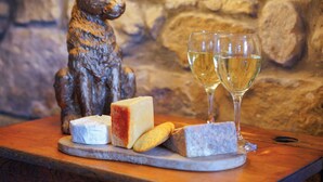 Une planche de fromages variés et de biscuits secs, accompagnée de deux verres de vin blanc, le tout présenté sur fond de mur en pierre.