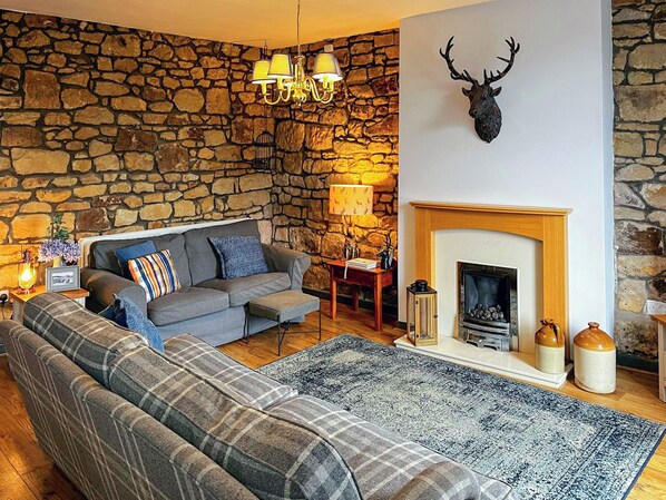 A cozy living room with a stone wall, a fireplace, a sofa, and a mounted deer head.