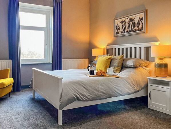 Una camera da letto ordinata con un letto, comodini, una finestra con tende e un quadro appeso al muro.