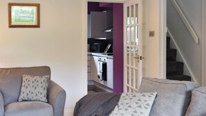 A living room with a grey sofa, a patterned pillow, and a knitted throw. A kitchen is visible through an open door with purple walls and white cabinets. - 2 bedroom accommodation in Horton-in-Ribblesdale, near Settle (Horton-in-Ribblesdale, near Settle)