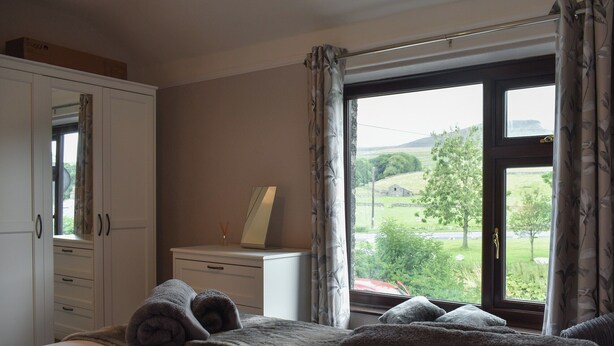 A bedroom with a bed, a dresser, a mirror, and a window with a view of a green landscape. - 2 bedroom accommodation in Horton-in-Ribblesdale, near Settle (Horton-in-Ribblesdale, near Settle)
