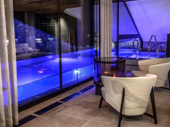 A modern spa area with a glass-enclosed hot tub, a fireplace, and comfortable seating.