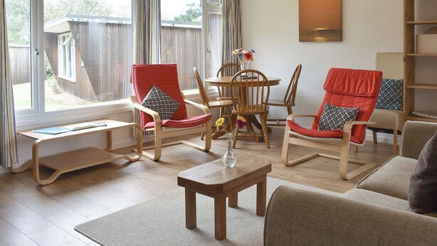 A living room with a wooden floor, a dining table with chairs, a sofa, and a bookshelf. - 2 bedroom accommodation in Mount Hawke, near Redruth (Mount Hawke, near Redruth)