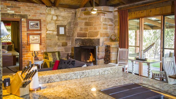 Une cheminée en pierre avec un feu de bois, un mur en pierre, un plafond en bois et une vue sur l’extérieur.