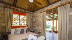 Une chambre avec un mur en pierre, un plafond en bois, un lit avec une literie blanche et une vue sur l’extérieur par une fenêtre.