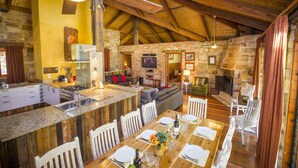 Une cuisine spacieuse dotée de plans de travail en granit, d’un coin repas avec des chaises blanches et d’une cheminée en pierre.