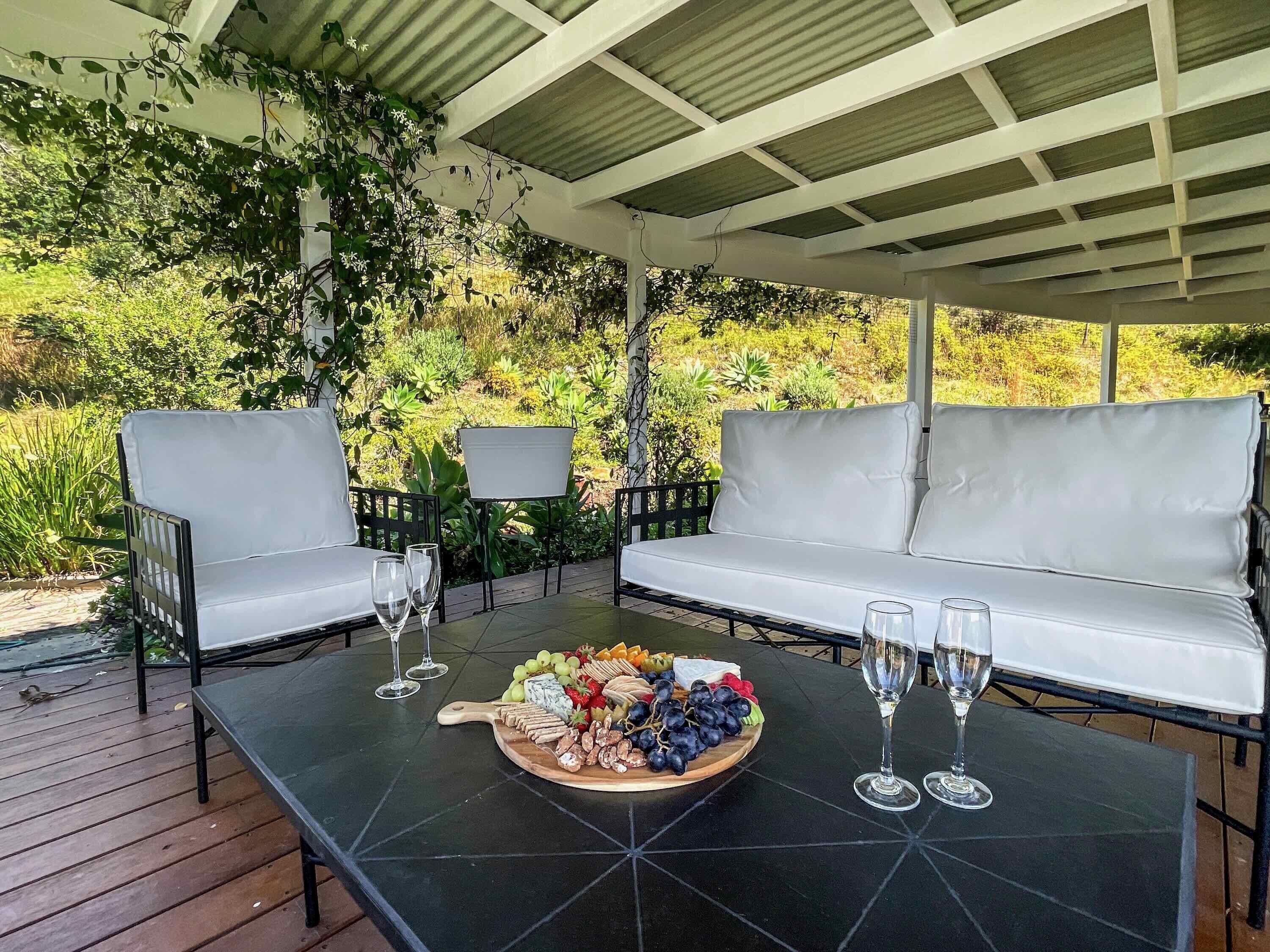 An outdoor seating area with a table set for a meal, surrounded by greenery.