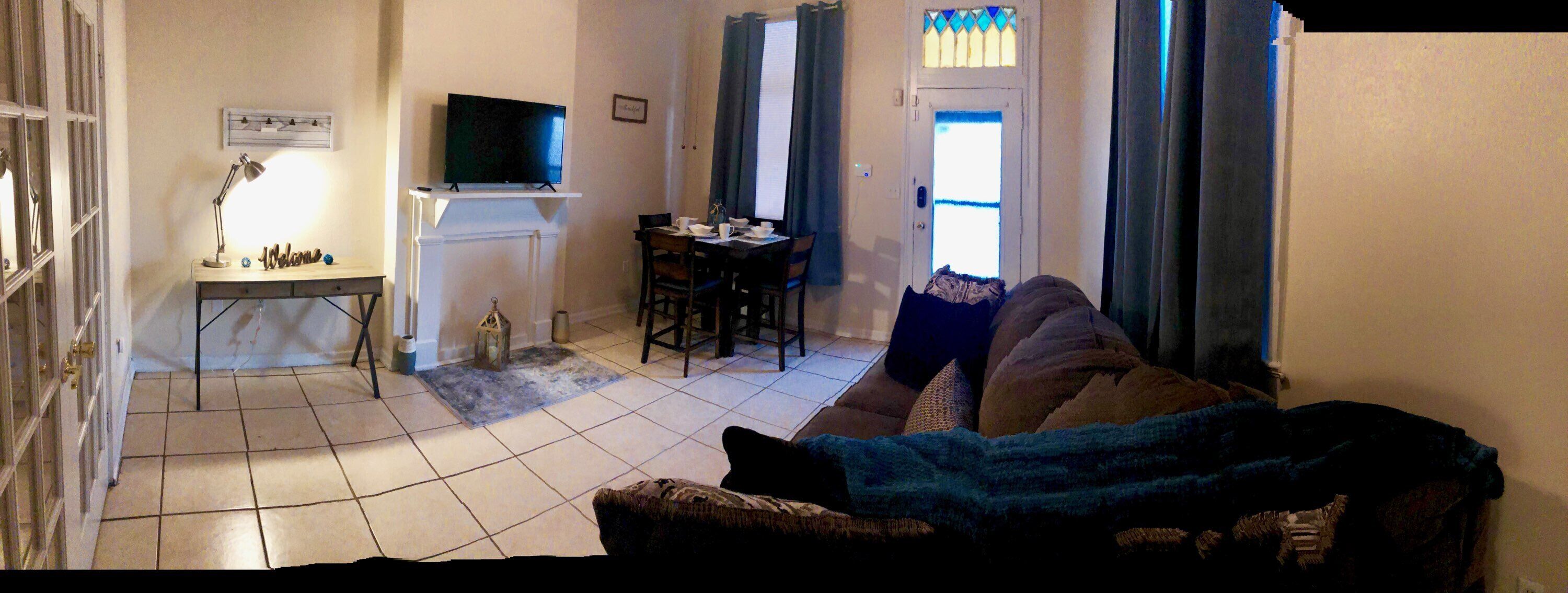 A living room with a TV on a stand, a dining table with chairs, and a sofa with a blanket.