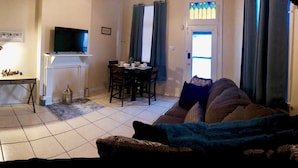 A living room with a TV on a stand, a dining table with chairs, and a sofa with a blanket.