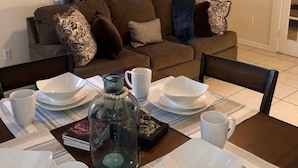 A dining area with a table set for four, including white plates, bowls, and cups. A decorative glass bottle is placed on the table.