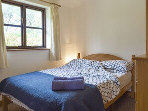 A single bed with a patterned bedspread, a wooden headboard, and a window with curtains.