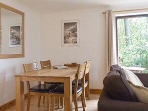 A dining area with a wooden table and chairs, a framed picture on the wall, and a window with a view of greenery. - Prince Croft Cottage - UK12560 (Mount Hawke, near Redruth)