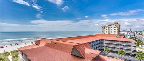 Un hôtel avec un toit rouge, donnant sur une plage et l’océan.