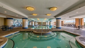 A large indoor swimming pool with multiple lanes, surrounded by lounge chairs and tables, and featuring a checkered column design.