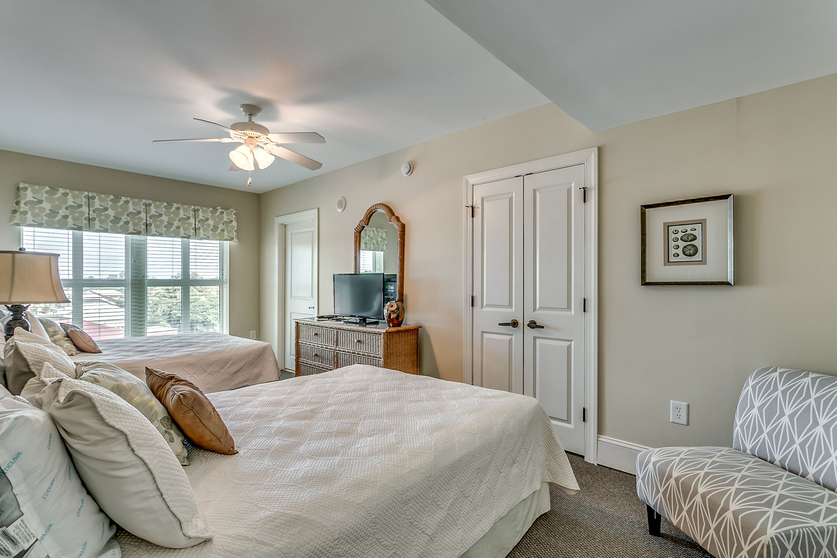 A bedroom with two beds, a ceiling fan, a dresser, a television, and a framed picture on the wall.