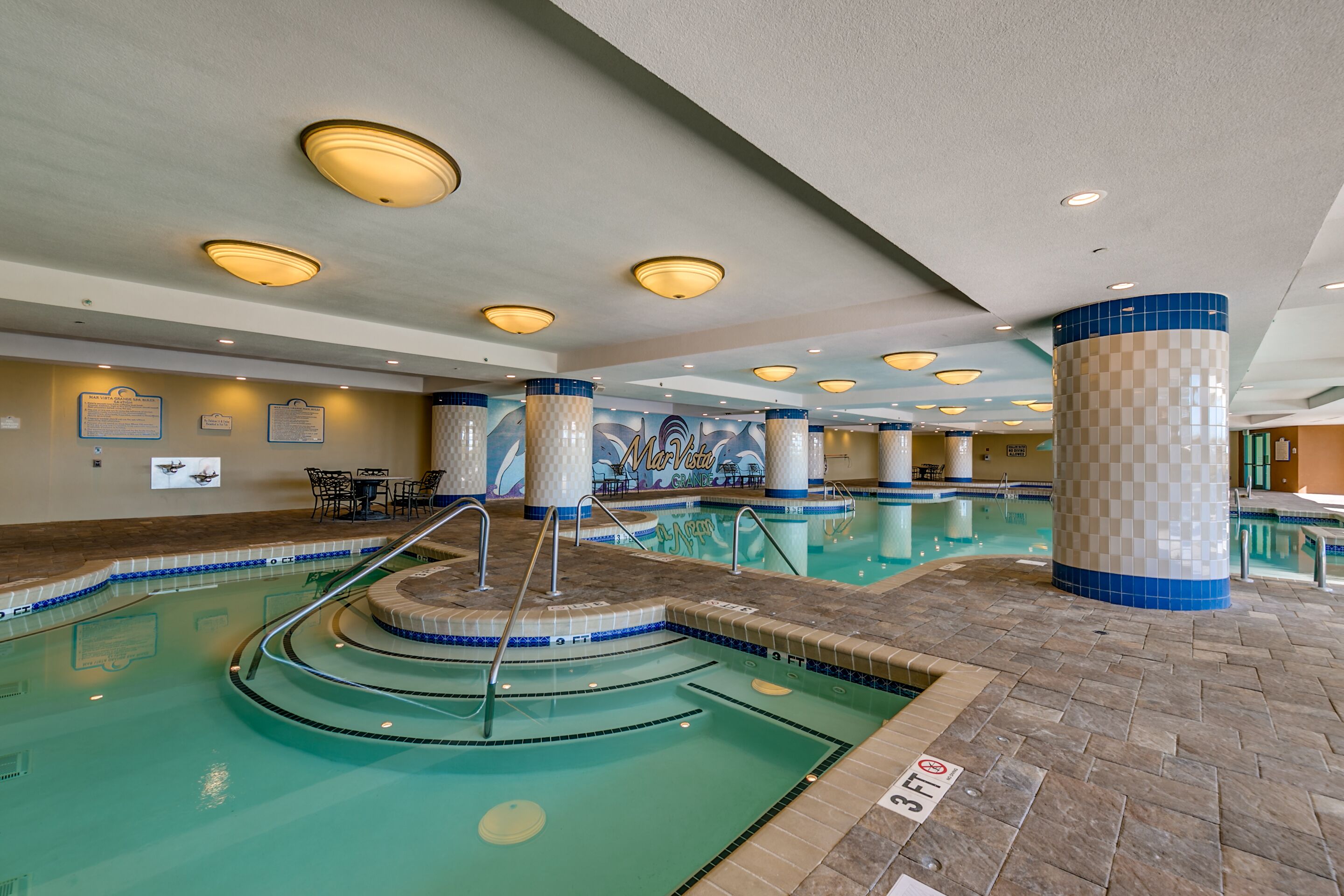 Una piscina interior con varias pistas de natación, una zona de estar con sillones y un mural en la pared.
