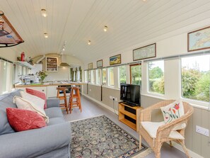 Un espacio habitable compacto con cocina, comedor y zona de estar, con ventanas amplias y una televisión.