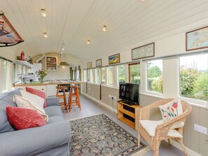 A compact living space with a kitchen, dining area, and seating area, featuring large windows and a television. - A truly beautiful train conversion, a stone’s throw from the River Test. (Horsebridge)