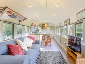 A cozy interior with a sofa, a TV, and a kitchen area. - A truly beautiful train conversion, a stone’s throw from the River Test. (Horsebridge)