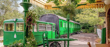 Un vagón de tren verde antiguo estacionado en un jardín, con un letrero de oficina de reservas, una mesa y sillas.