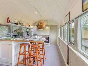 A modern kitchen with a central island, bar stools, a built-in oven, and a window with a view. - A truly beautiful train conversion, a stone’s throw from the River Test. (Horsebridge)