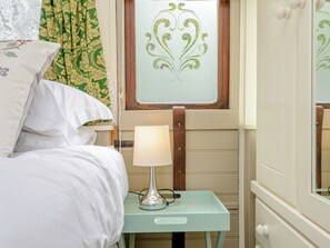 A bed with white bedding, a bedside table with a lamp, and a window with a decorative glass panel. - A truly beautiful train conversion, a stone’s throw from the River Test. (Horsebridge)