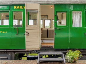 A green train carriage with a door labeled 'RAILWAY FIRST' and a window with a map. - A truly beautiful train conversion, a stone’s throw from the River Test. (Horsebridge)