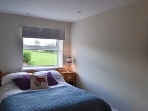 Un dormitorio con cama, mesita de noche, lámpara y ventana con vista a un campo verde.