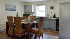 Un comedor con sillas de mimbre, una mesa de madera y una cocina al fondo.