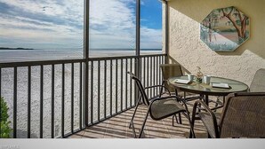 A balcony with a view of the ocean, a round table with chairs, and a ceiling fan. - Fort Myers Beach front Condo with amazing view of Gulf (Fort Myers Beach)