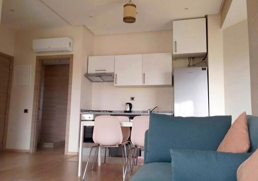 Een moderne keuken met witte kasten, een inbouwoven en een koelkast. Er is een eethoek met een tafel en stoelen.