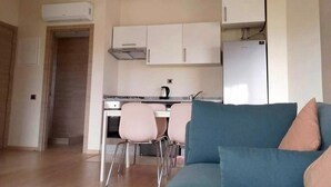 Moderni keittiö, jossa on valkoiset kaapit, sisäänrakennettu uuni ja jääkaappi. Keittiössä on myös ruokailutila, jossa on pöytä ja tuolit.