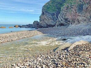 Una playa rocosa con agua cristalina, piedras y un acantilado.