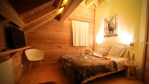 A cozy wooden cabin bedroom with a bed, a chair, a small table, and a television on a shelf. - Spacieux Chalet, proche des Télésièges,  Terrasse (Valloire)