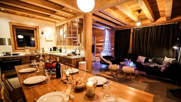 A wooden interior with a dining area set for a meal, a cozy living area with a couch and a fireplace, and a kitchen with modern appliances. - Spacieux Chalet, proche des Télésièges,  Terrasse (Valloire)
