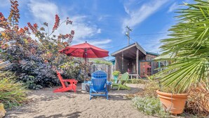 A sandy outdoor area with a red umbrella, a blue chair, and a green chair. - Cute & Colourful Oceanside Cottage w Garden (Stinson Beach)