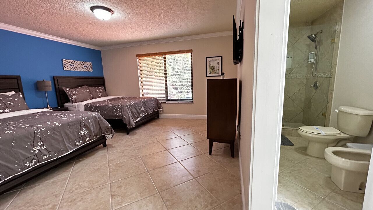 Een slaapkamer met twee bedden, een raam met jaloezieën, een nachtkastje en een kledingkast.