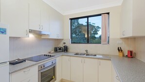 Una cucina moderna con mobili bianchi, forno a incasso, piano cottura, lavello e una finestra vista alberi.