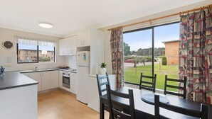 A modern kitchen with white cabinets, a built-in oven, and a dining area with a table and chairs. - Apollo Unit 17 - Ground Floor (Narooma)