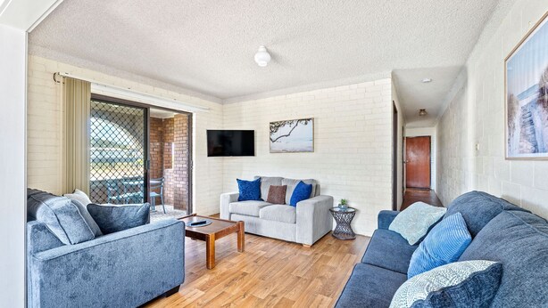 A spacious living area with a sofa set, a coffee table, and a TV mounted on the wall. - Apollo Unit 20 - Ground Floor (Narooma)