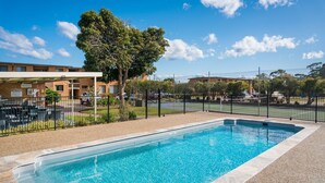 A swimming pool with a surrounding fence, a covered patio area with outdoor seating, and a building in the background. - Apollo Unit 20 - Ground Floor (Narooma)