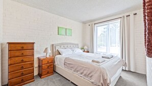 A bedroom with a bed, a wooden dresser, and a window with curtains. - Apollo Unit 20 - Ground Floor (Narooma)