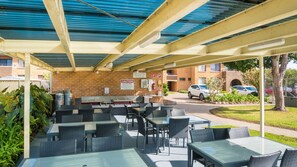 Un patio al aire libre con mesas y sillas, una pared de ladrillo y una sección cubierta con techo de metal.