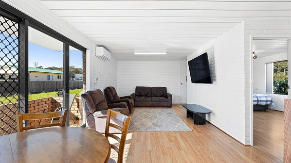 Un patio moderno con una mesa de comedor, dos sofás y un televisor montado en la pared.