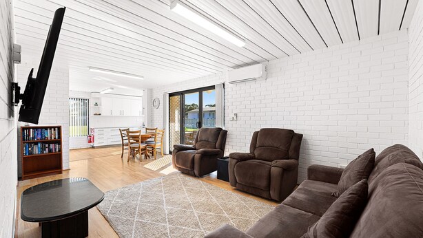 Ein modernes Wohnzimmer mit einer weißen Ziegelwand, einem schwarzen Ledersofa, einem braunen Relaxsessel und einem Essbereich mit Holzmöbeln.