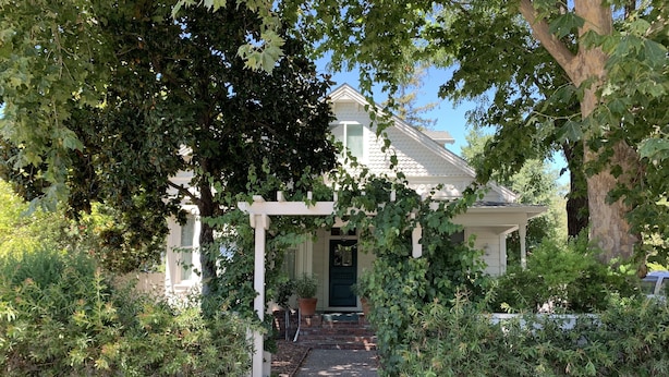 A house with a covered porch, a gravel pathway leading to the front door, and a variety of plants and shrubs around the property.