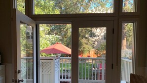 A view through a glass door into a backyard with a wooden deck, a red umbrella, and a white fence.
