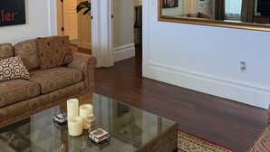 A living room with a sofa, a glass coffee table, and a large mirror.