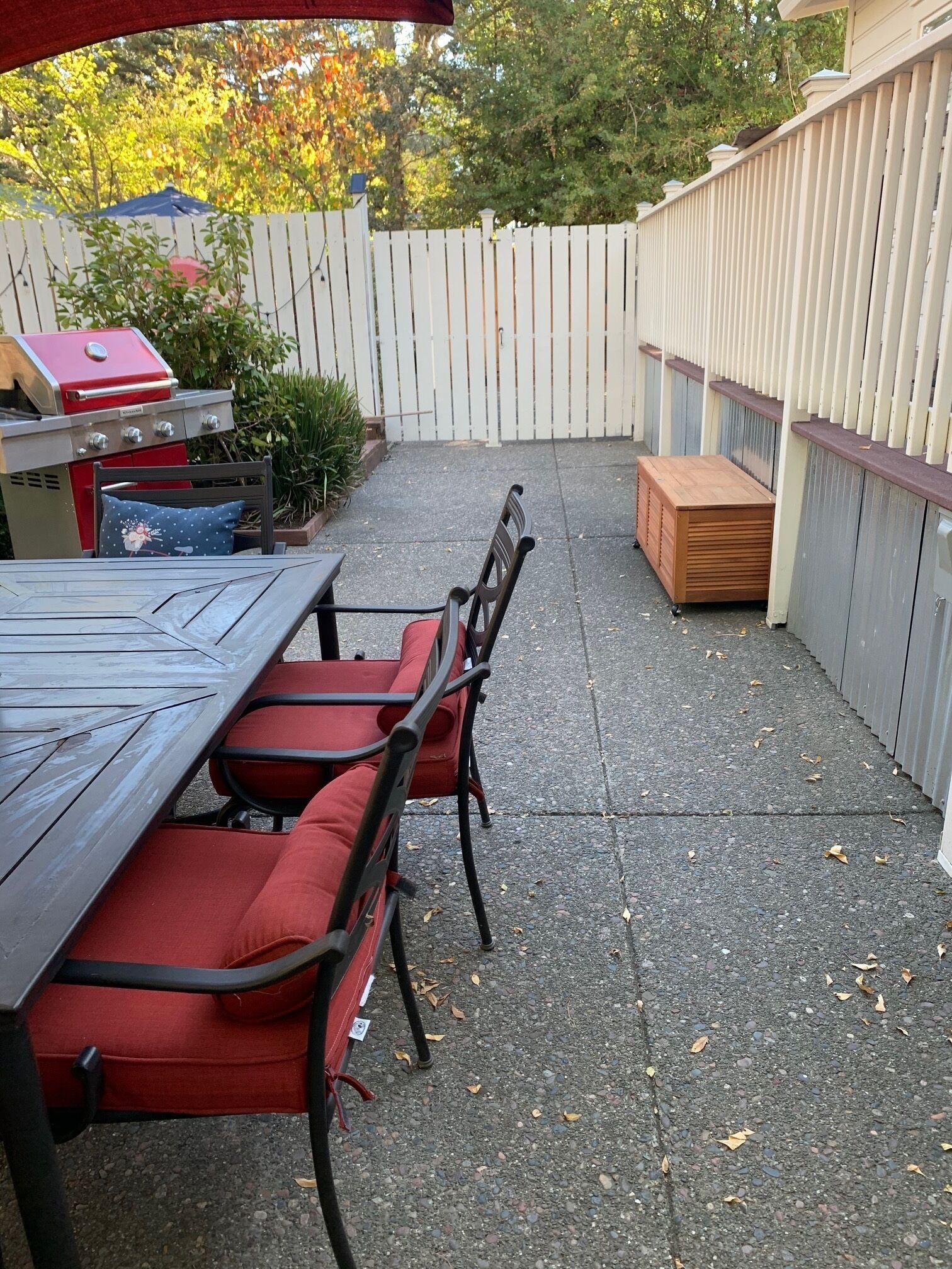 Eine Terrasse mit einem Holztisch, roten Sitzgelegenheiten, einem Grill und einem weißen Zaun.
