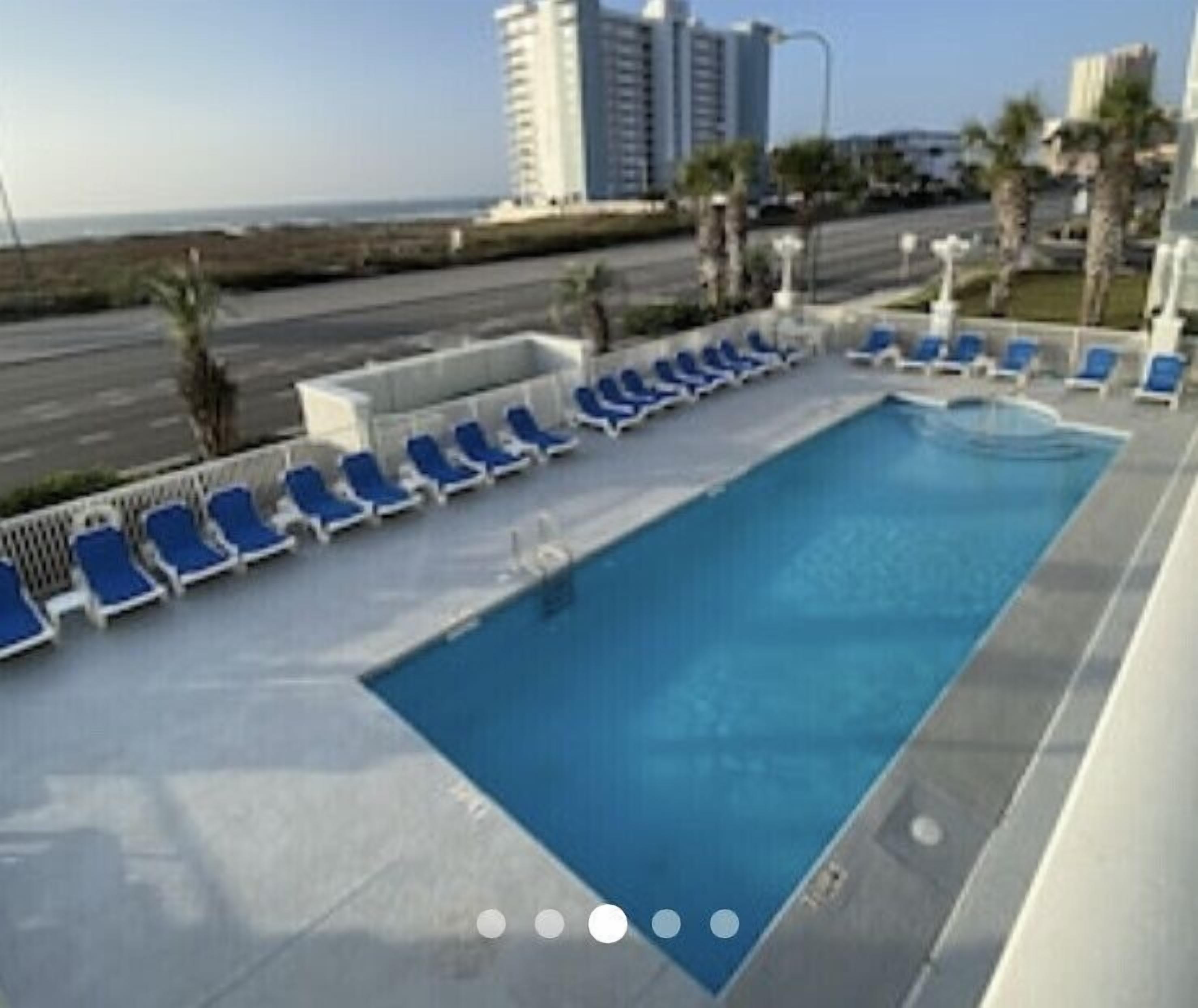 A swimming pool with blue lounge chairs and a view of the ocean and buildings in the background.